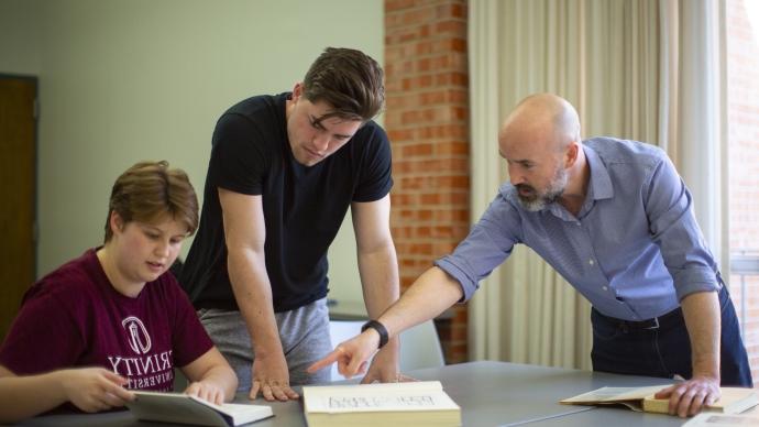 chad spigel pointing at a book next to two students